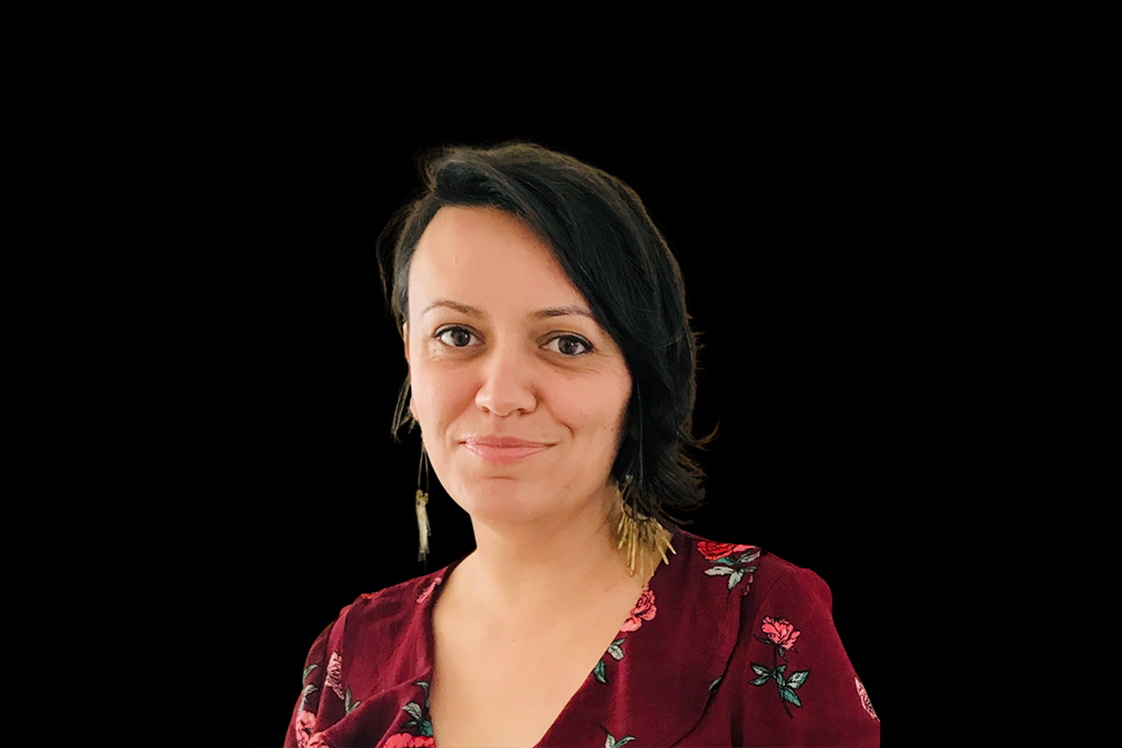 Image of General Manager Kiri Zakinthinos. Kiri stands against a black background and wears a v neck floral top. She has short dark hair and long earrings and smiles at the camera.